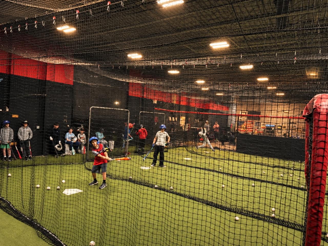 A hitter mid swing in a long cage, players waiting their turn